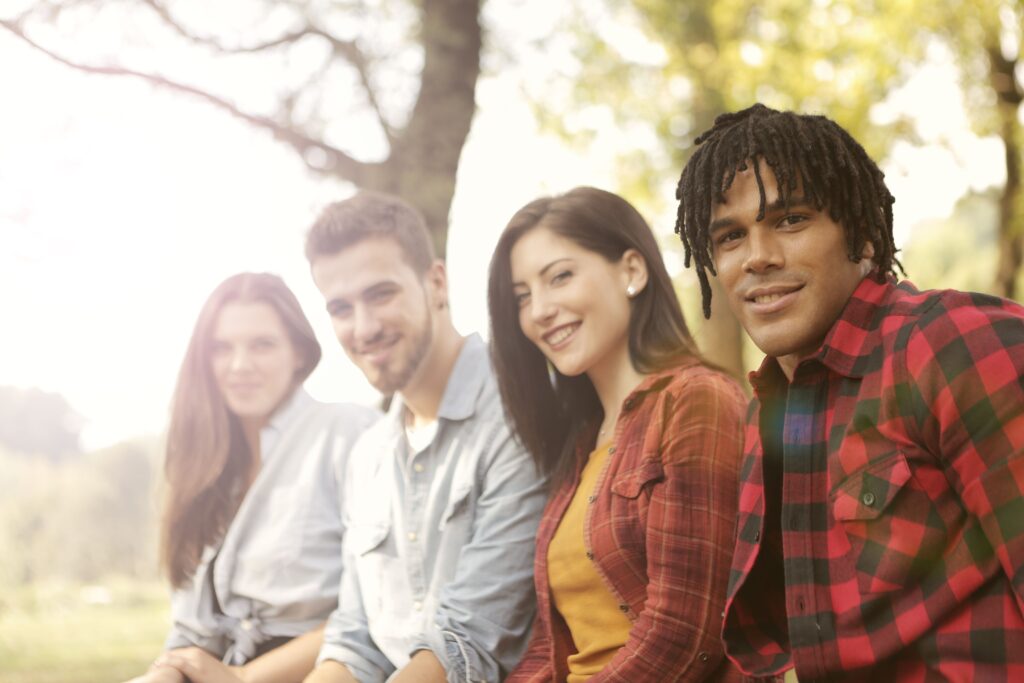 A diverse group of friends sitting outdoors, smiling and enjoying a sunny day.