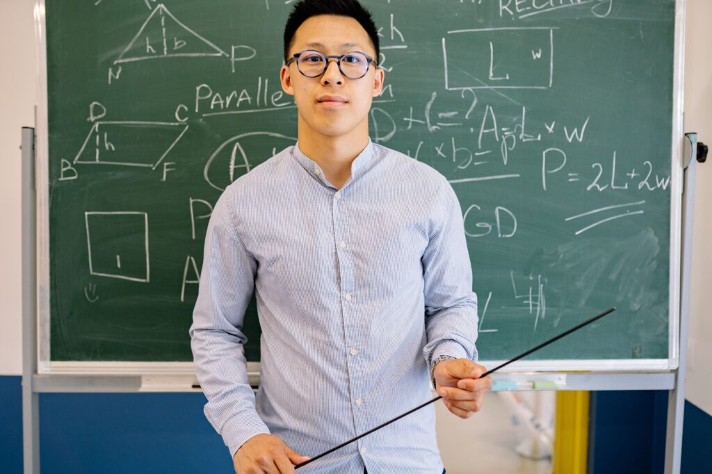 Confident teacher stands with pointer in front of a chalkboard filled with mathematical equations for a lesson.